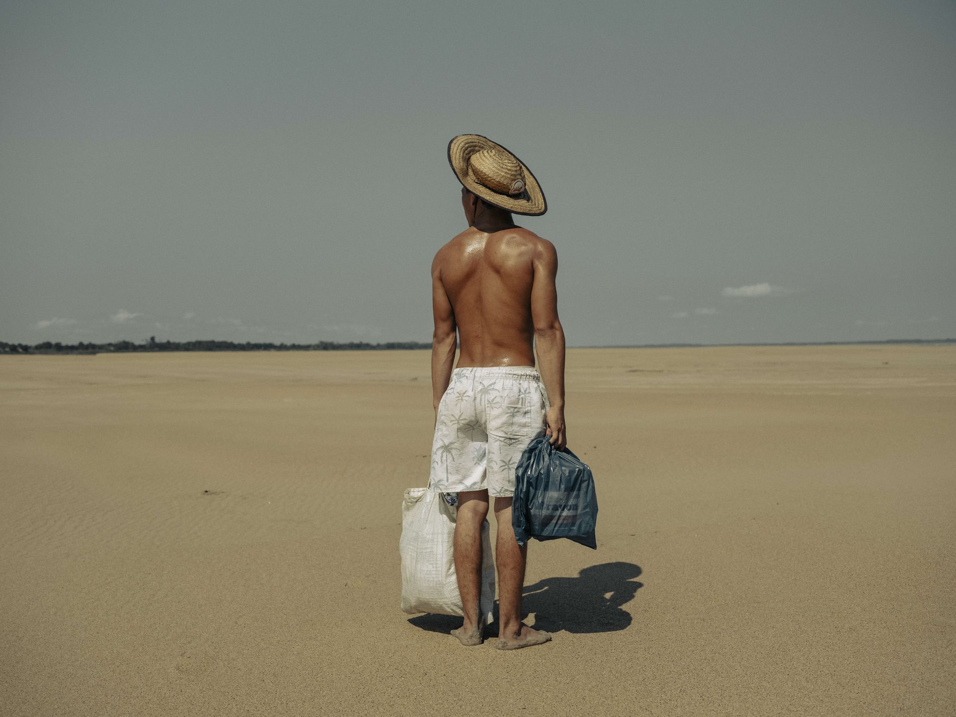 A young man brings food to his mother who lives in the village of Manacapuru, Amazonas, Brazil. The village was once accessible by boat, but because of the drought, he must walk two kilometers along the dry riverbed of the Solimões River to reach her.&nbsp;