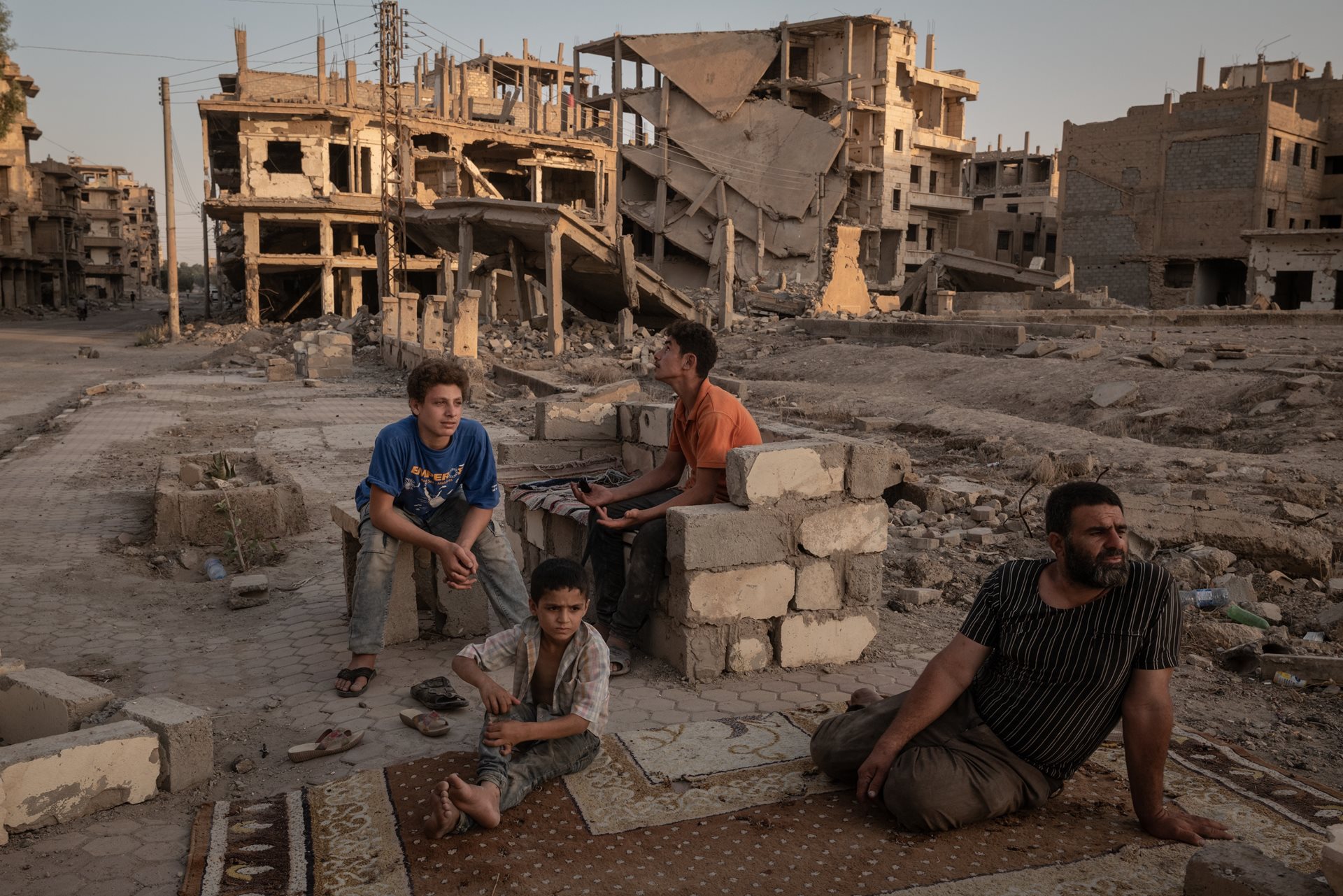 Abdelatif Daham Al Hummada (right) sits with his sons and nephew on the street outside their heavily damaged home, where the family often sleeps, in Deir al-Zour, Syria.